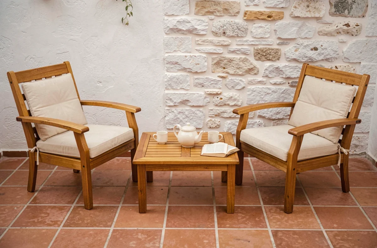 Deux fauteuils de jardin en teck avec accoudoirs autour d'une table basse sur un patio méditerranéen en carreaux de terre cuite avec théière et tasses en céramique
